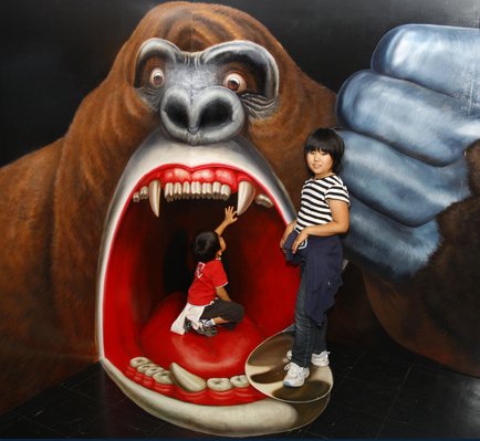 two kids standing by a painting of a gorilla, with perspective such that the gorilla looks like it's eating them