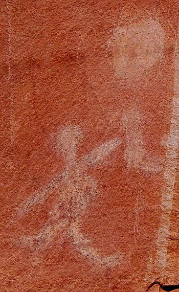 rock art showing a human figure holding a baby up to a solar symbol