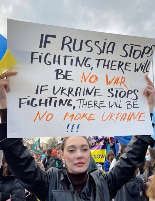 woman holding sign that says 'If Russia stops fighting there will be no war. If Ukraine stops fighting there will be no more Ukraine!!