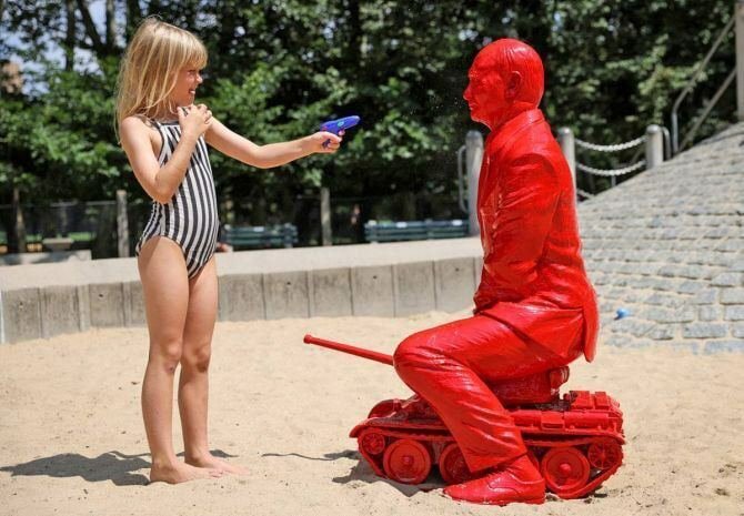 small statue of Putin sitting on a tank, a young girl is aiming a water pistol at it