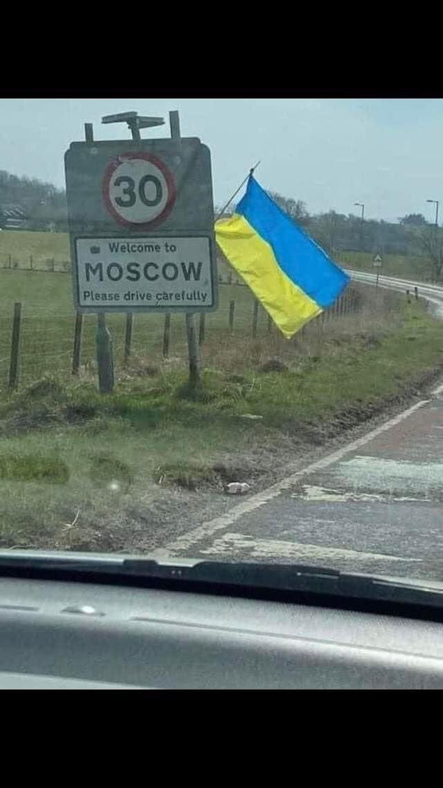 highway sign saying 'Welcome to Moscow' with a Ukrainian flag hung on it